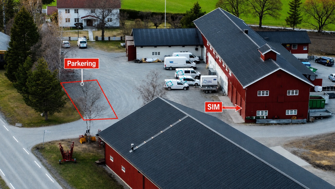 Flyfoto av Stafsbergvegen 167: merket parkering til venstre ved innkjørselen, og inngang til simulatoren (SIM) i den røde låven